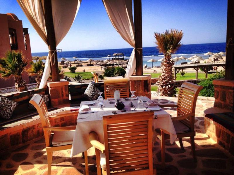 Terrace with set table and chairs overlooking palm trees and the sea.