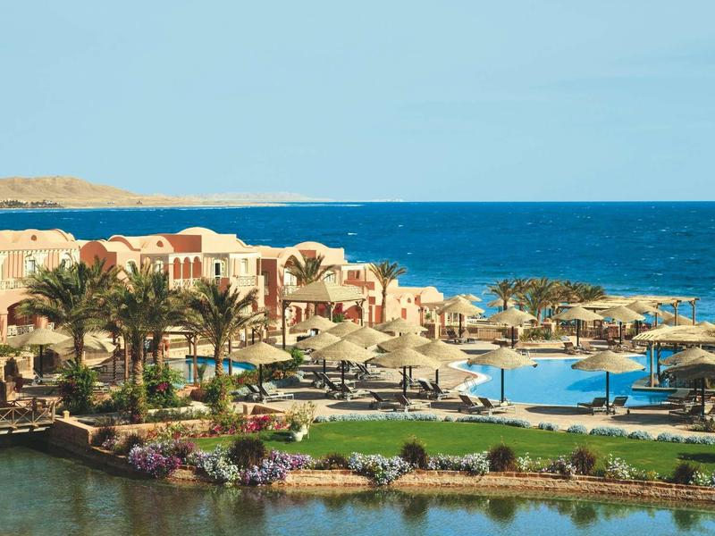Luxury hotel resort with pool and sea view, surrounded by palm trees and gardens.