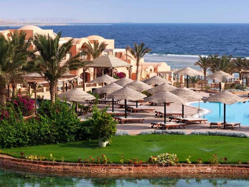Hotel resort with pool, sun loungers, palm trees, and sea in the background