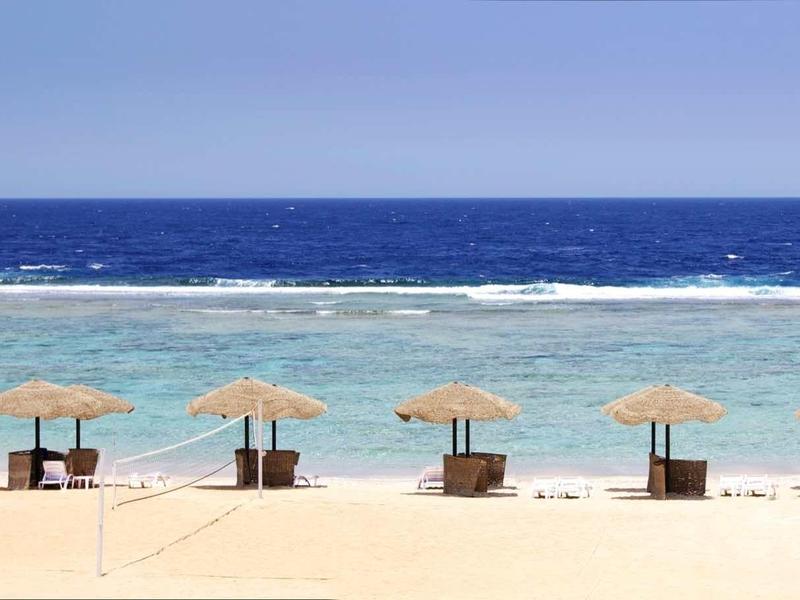 Sandy beach with parasols and chairs by clear blue sea and sky.