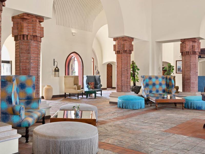 Großer, heller Hotel-Loungebereich mit bunten Sesseln und Säulen aus Ziegeln.