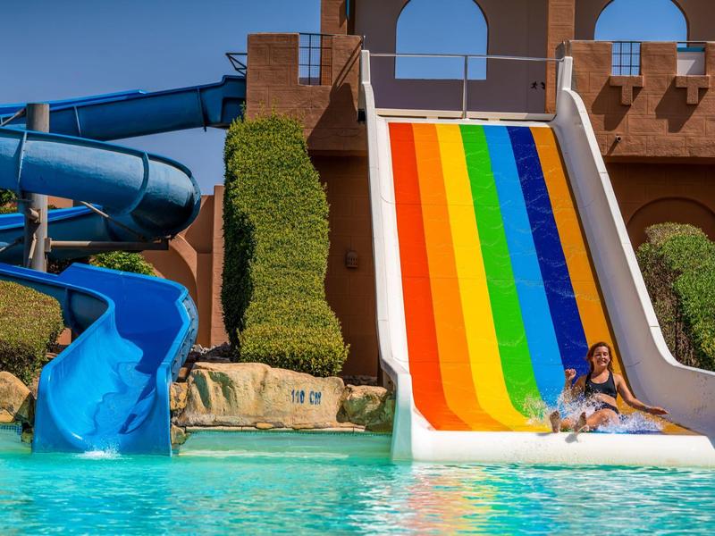 Kleurrijke brede glijbaan naast blauwe buisglijbaan met kind in zwembad voor hotel.