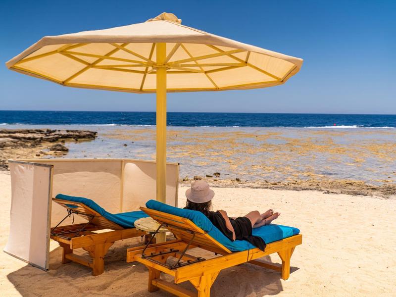 Persoon ontspant op ligstoel onder parasol aan het strand met zeezicht.