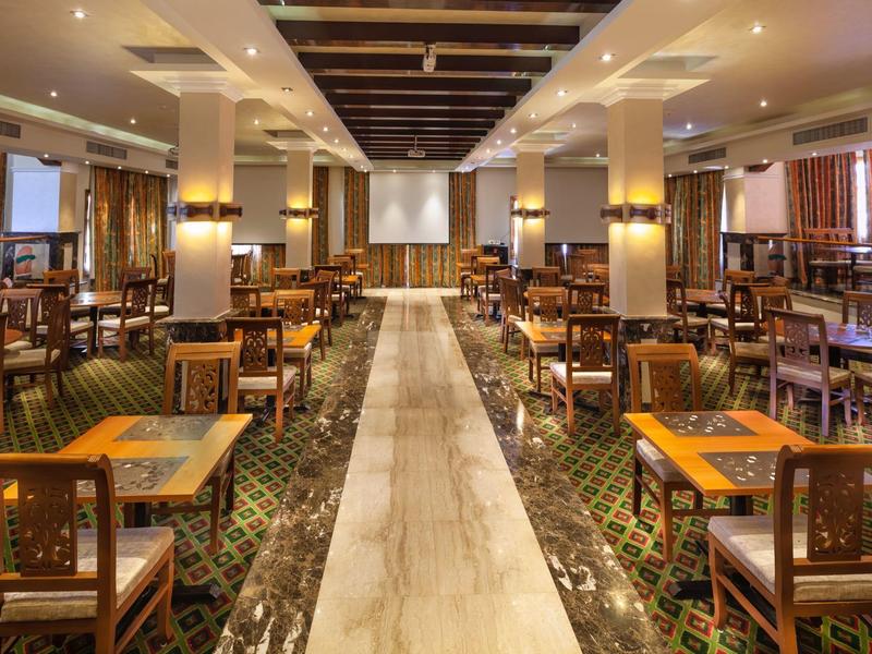 Grote eetzaal met houten tafels en stoelen, marmeren vloer en gedempte verlichting.