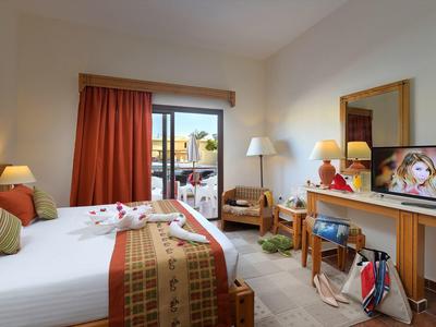 Helles Hotelzimmer mit Doppelbett, Balkon, Schreibtisch, Fernseher und warmen Holzmöbeln.