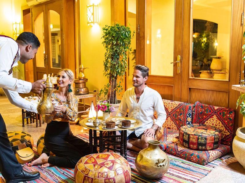 Koppel geniet van drankjes terwijl een ober hen serveert in een warm verlichte lounge met kleurrijke kussens.