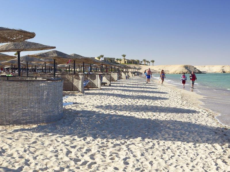 Strand met parasols, stoelen en mensen die lopen nabij turquoise zee onder een heldere lucht.