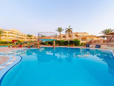 Großer Hotelpool mit Sonnenterrasse und Palmen bei klarem Himmel.