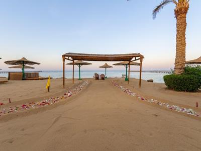 Sandweg zum Strand mit Pavillon, Palmen und Sonnenschirmen am Meer.