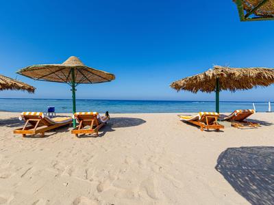 Leerer Sandstrand mit Liegestühlen und Strohmännern unter klarem blauem Himmel