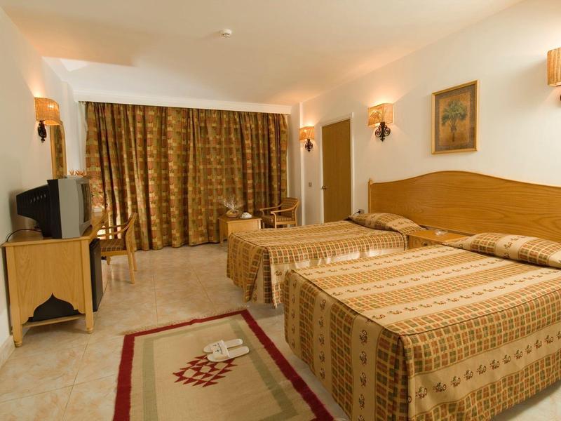 Hotelzimmer mit zwei Einzelbetten, Holzmöbeln, Teppich und goldfarbenen Vorhängen.