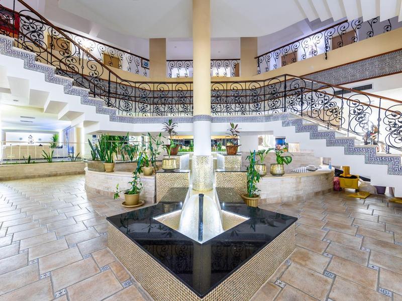 Großer heller Innenraum mit zweistöckiger Wendeltreppe, Pflanzen und modernem Brunnen in der Mitte.