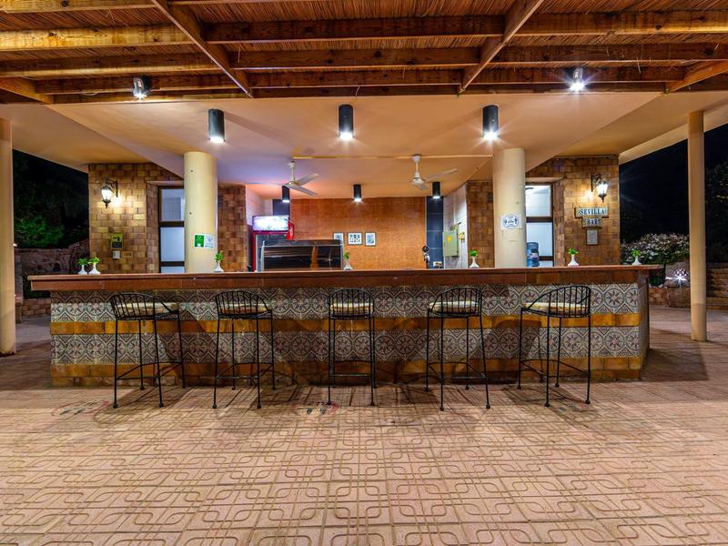 Offene Bar mit hohem hölzernem Dach, Steinverkleidung und sieben hohen Metallstühlen davor.