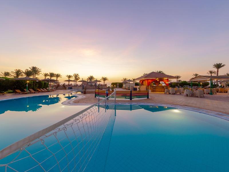 Großer Pool mit klarstem Wasser, umgeben von Liegestühlen und Palmen bei Sonnenuntergang.