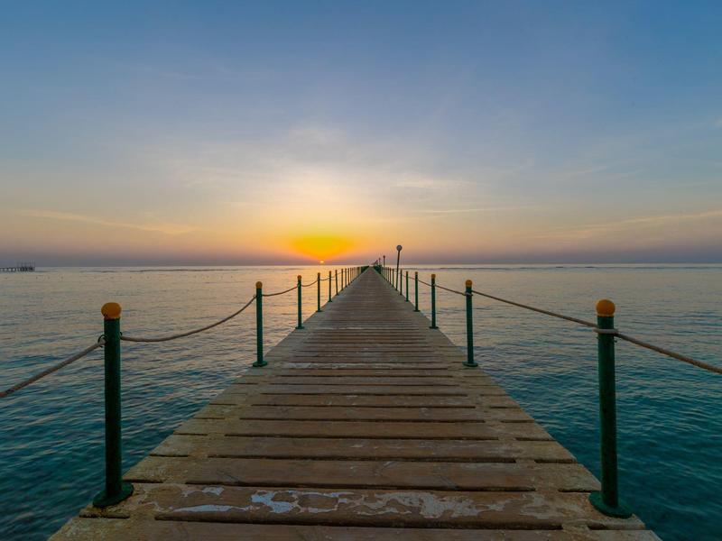 Ein langer Steg aus Holz führt ins ruhige blaue Meer bei Sonnenuntergang.