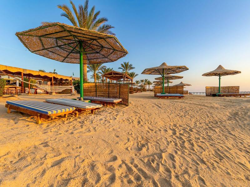 Leerer Sandstrand mit Sonnenschirmen und Liegen bei klarem Himmel und warmem Sonnenlicht.