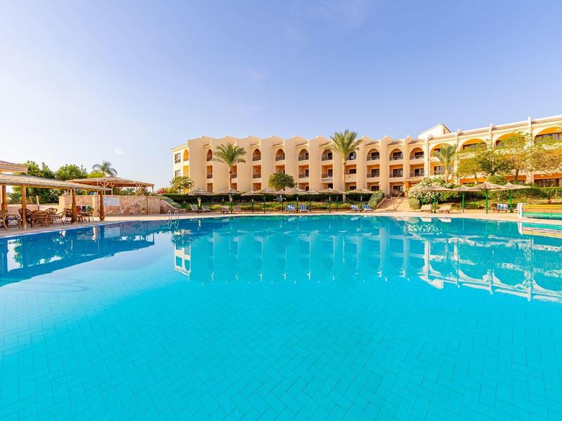 Großer blauer Pool mit umliegendem Hotelgebäude unter klarem Himmel.