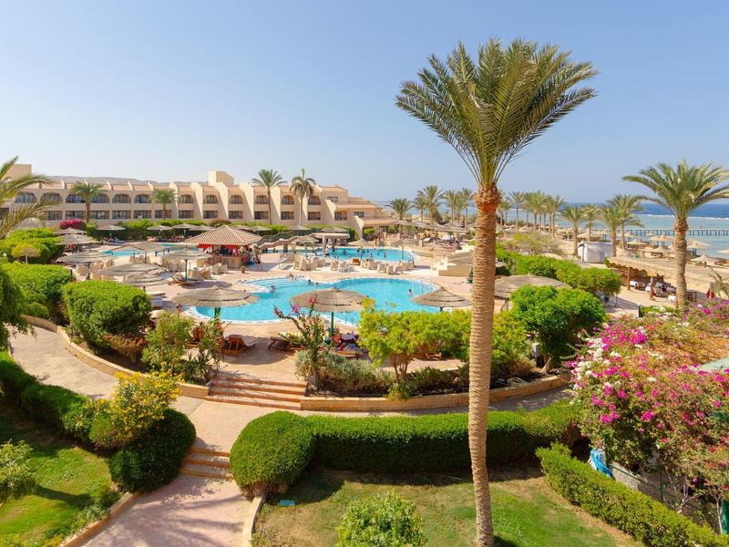 Große Hotelanlage mit mehreren Pools, Palmen, grünen Gärten und Blick auf das blaue Meer.