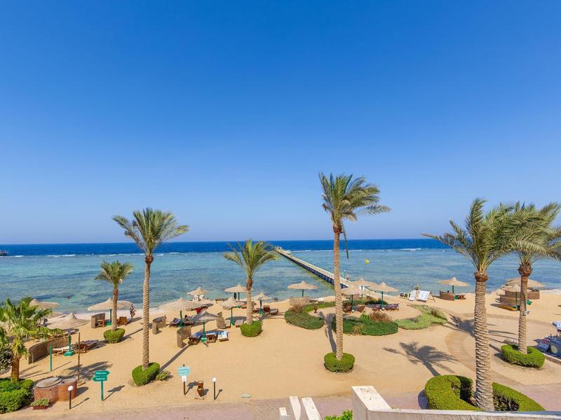 Strand mit Palmen, blauer Himmel und ruhig klarblauem Meer, Liegestühle und Sonnenschirme am Sand.