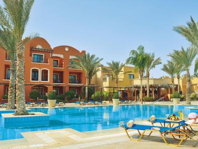 Hotelpool mit Liegestühlen, Palmen und mehrstöckigen Gebäuden im Hintergrund bei klarem Himmel