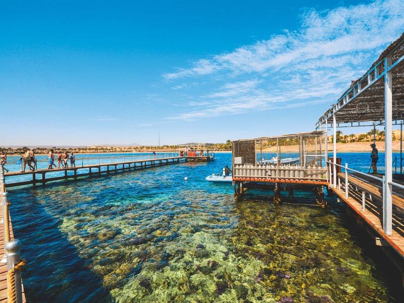 Helder turquoise water met pier en zonnescherm onder een heldere blauwe lucht.