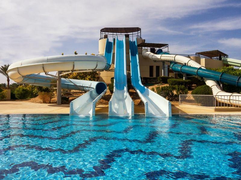 Waterpark met drie glijbanen die uitkomen in een groot zwembad onder een heldere lucht.