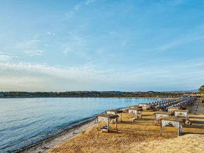Strand mit Holzliegen am ruhigen Meer unter blauem Himmel und leicht bewölkter Atmosphäre.
