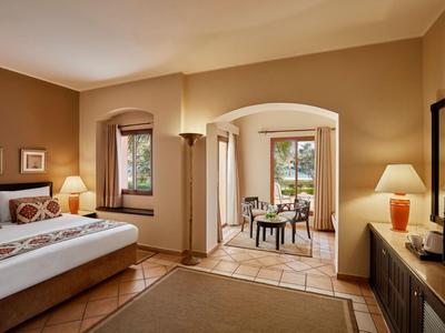 Gemütliches Hotelzimmer mit Doppelbett, zwei Fenstern, Teppichboden und angrenzendem Balkon mit Sitzgruppe.