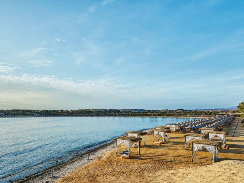 Sandy beach with lounge chairs and umbrellas along calm water under a blue sky.