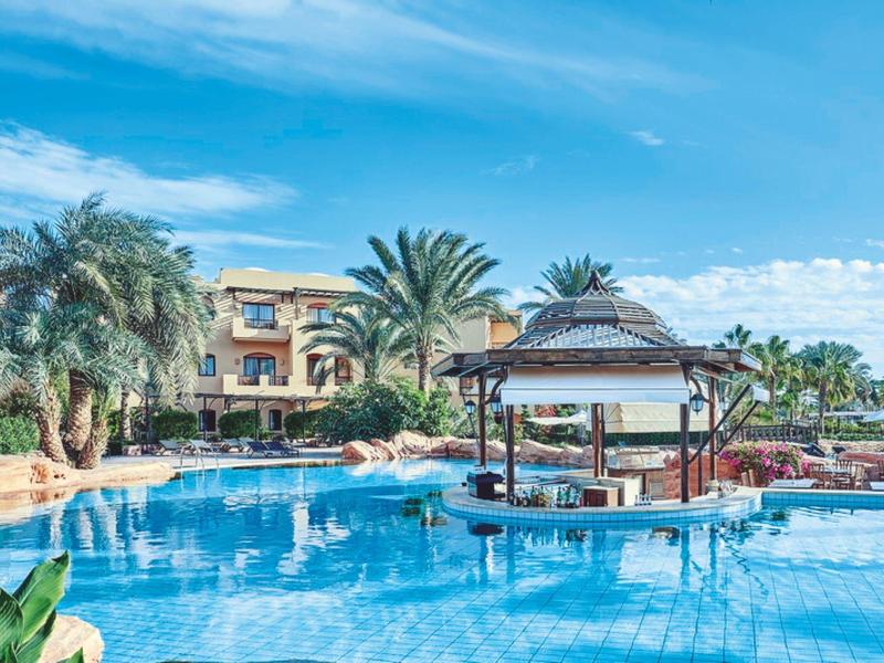 Resort with a large swimming pool, palm trees, and a swim-up bar under a gazebo.