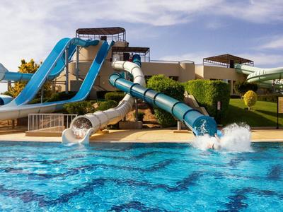 Wasserpark mit drei Wasserrutschen mündet in ein großes blaues Schwimmbecken.