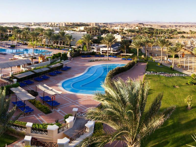 Large hotel pool area with sun loungers and palm trees in daylight.