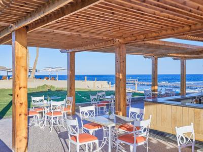 Überdachte Terrasse mit weißen Stühlen und Tischen mit Blick auf den Strand und das Meer.