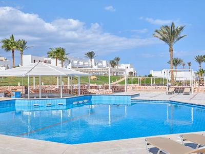 Großer Außenpool mit Liegestühlen und Palmen bei sonnigem Wetter in einem Hotelresort.