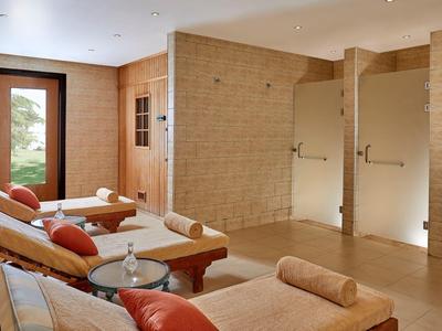 Innenraum mit drei Glasduschen, hellbraunen Liegen und roten Kissen, heller Raum mit Holztüren.