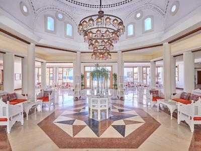 Großer, heller Saal mit Runddach, Kronleuchter und symmetrisch angeordneten weißen Sitzgruppen.