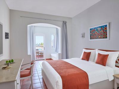 Hell eingerichtetes Hotelzimmer mit Doppelbett und Zugang zu einem Balkon mit Meerblick.