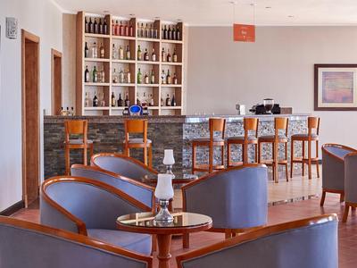 Moderner Hotelbarraum mit Ledersesseln, Holztheke, Hochstühlen und Regal mit Spirituosen.