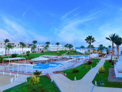 Große Poolanlage mit mehreren Pools, Grünflächen und weißen Gebäuden unter blauem Himmel.