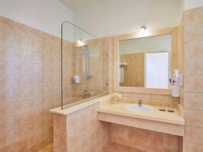 Helles Badezimmer mit beiger Glasdusche, großem Spiegel, Waschbecken und wandmontiertem Föhn.