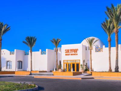 Weißes Eingangsgebäude mit Palmen und klar blauem Himmel.