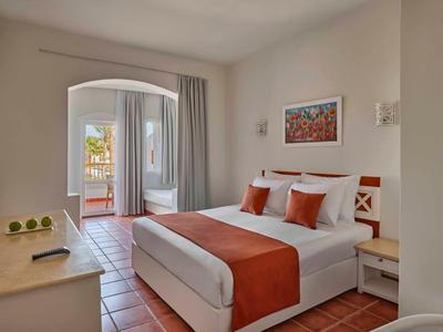 Helles Schlafzimmer mit Doppelbett, weiß-orange Bettwäsche, Balkon und Fliesenboden.