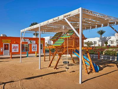 Kinderspielplatz mit Holzgerüst, Rutsche, Sandboden und weißem Sonnenschutzdach bei klarem Himmel.