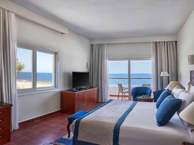 Helles Schlafzimmer mit großem Fenster, Meerblick, Doppelbett und Holzmöbeln.