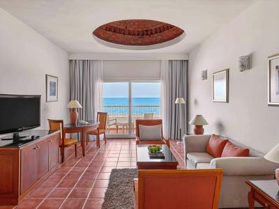 Helles Wohnzimmer mit Terrakottafliesen, roten Möbeln und Meerblick durch große Fenster.