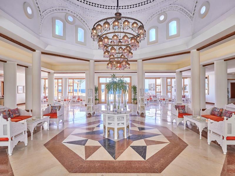 Großer, heller Saal mit Runddach, Kronleuchter und symmetrisch angeordneten weißen Sitzgruppen.