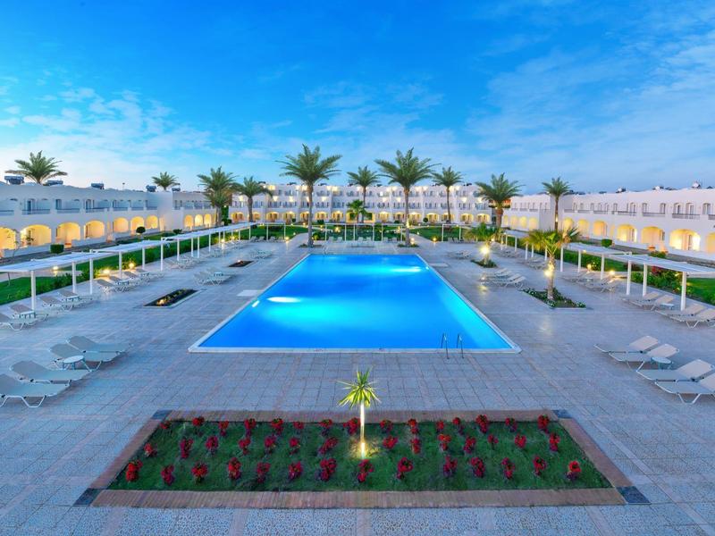 Großer rechteckiger Pool in modernem Hotel mit Palmen, Liegestühlen und blauem Himmel.