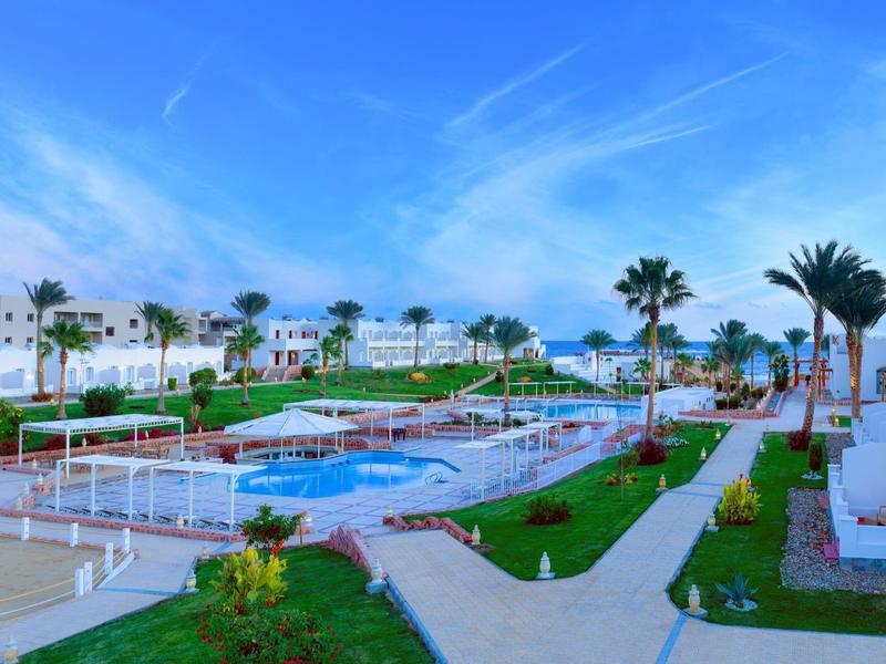 Große Poolanlage mit mehreren Pools, Grünflächen und weißen Gebäuden unter blauem Himmel.