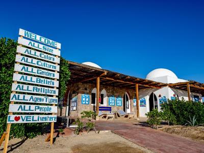 Eingangsbereich eines Hotels mit Holzschild und weißem Gebäude unter klarem blauem Himmel