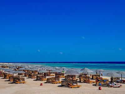 Strand mit Reihen von Liegestühlen und Sonnenschirmen am blauen Meer unter klarem Himmel.